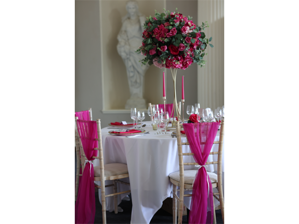 Elegant table setting with tall pink floral centrepiece and chairs tied with fuchsia sashes