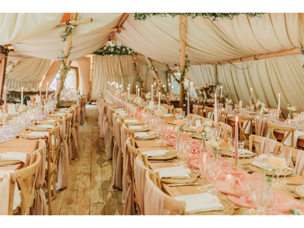 Long banquet tables set for a wedding reception inside a draped marquee with candles and blush table runners