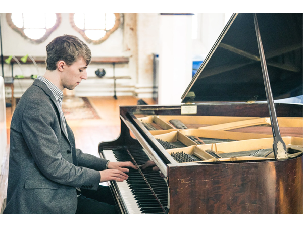 Young man playing a grand piano in a bright room