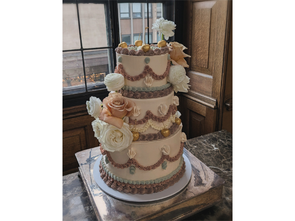Three-tier wedding cake with blush and white roses on a silver stand by a window