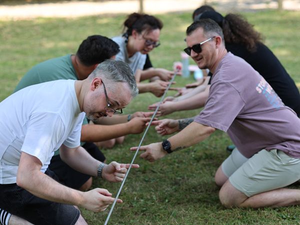 Group of adults kneeling on grass during a team-building activity, holding strings and concentrating