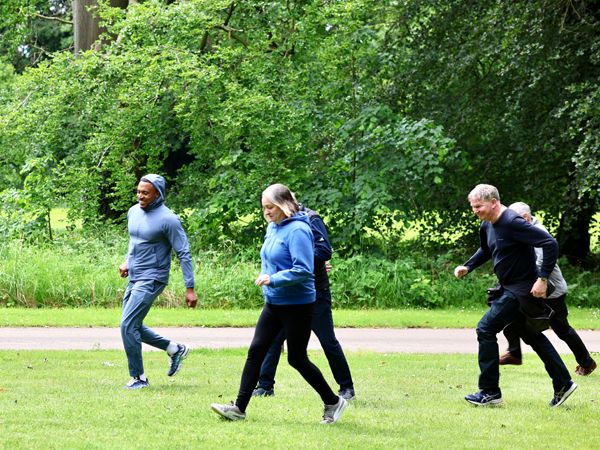 A group of adults walking briskly across a grassy park with trees in the background.