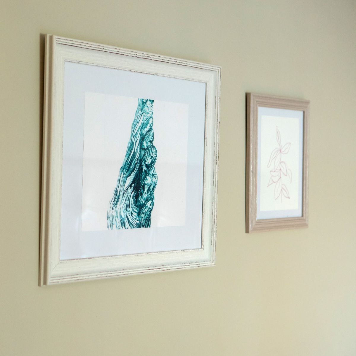 Three framed pictures hanging on a beige wall, featuring botanical sketches and an abstract artwork.