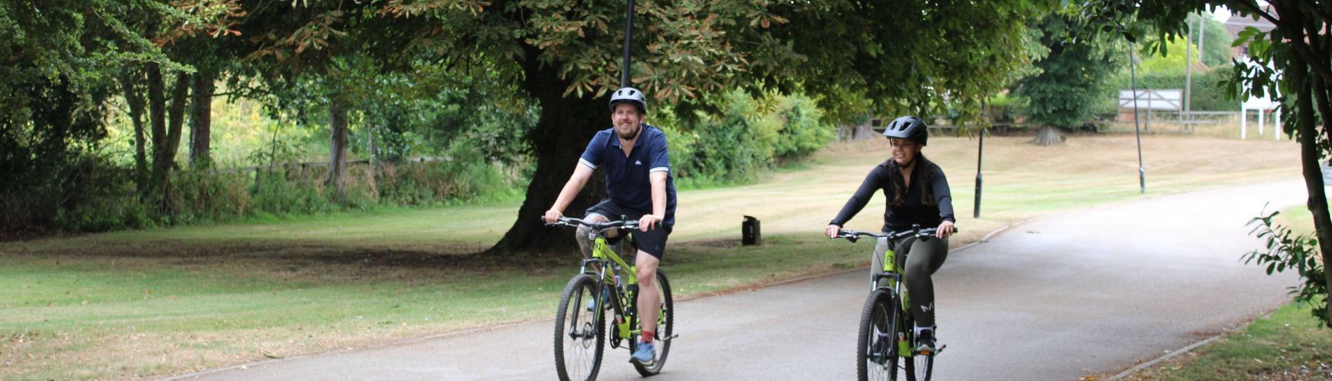 Two people riding bicycles on a paved path surrounded by greenery and trees