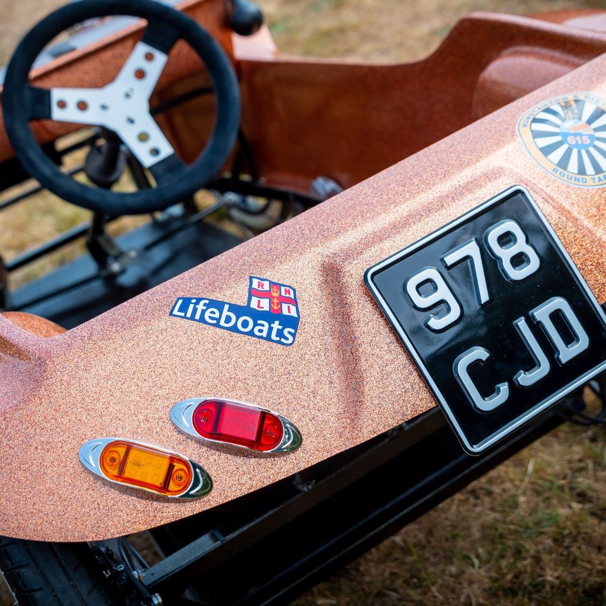 Close-up of a soap box derby car with a steering wheel, black license plate, and Lifeboats sticker.