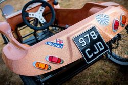 Close-up of a soap box derby car with a steering wheel, black license plate, and Lifeboats sticker.