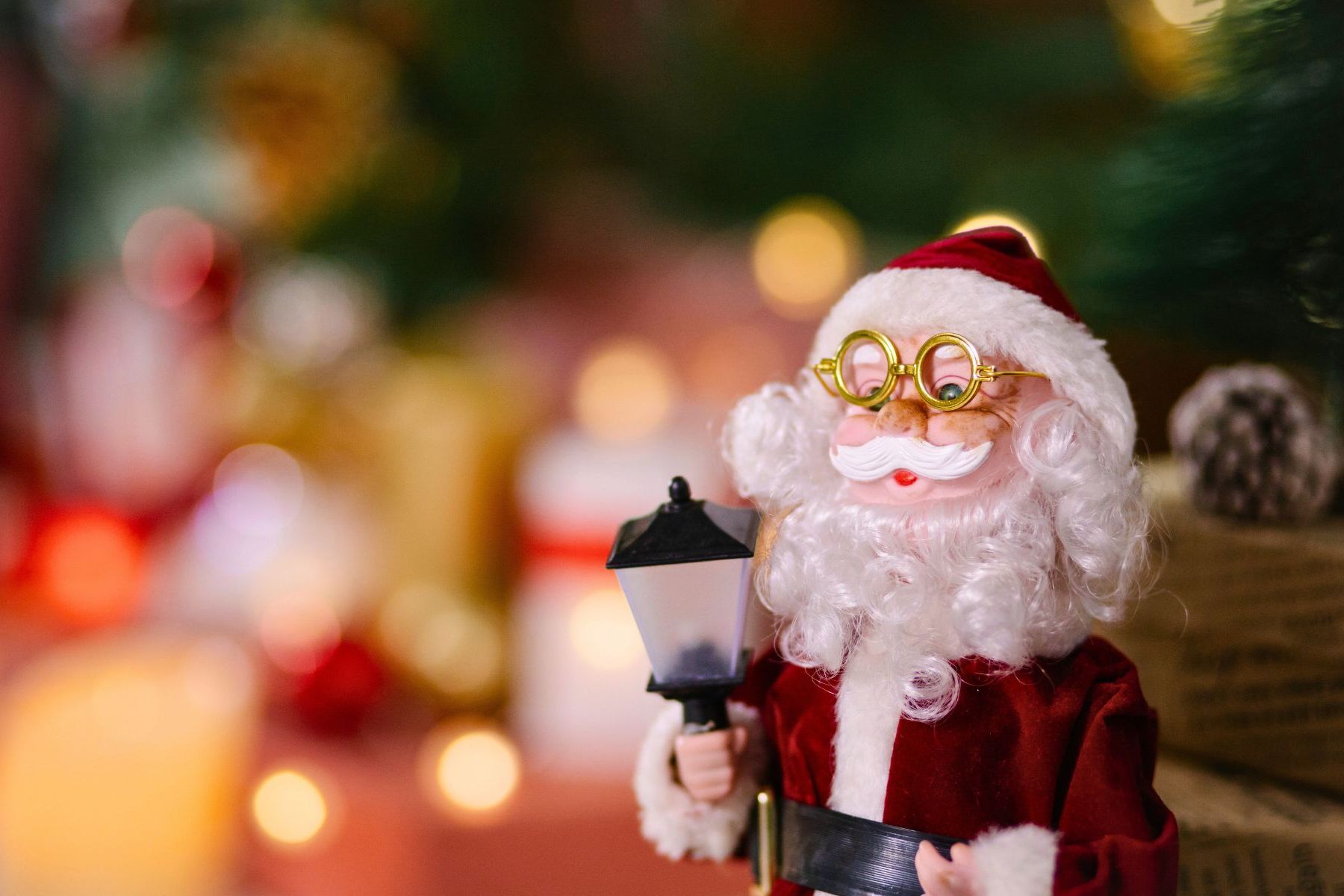 Santa Claus figurine holding a lantern with Christmas decorations in the background