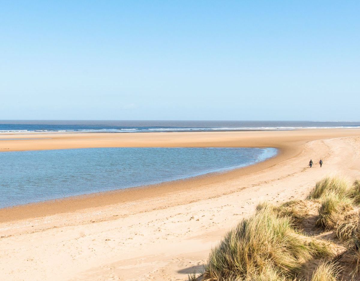 Sandy beach with grassy dunes and blue sky at the Norfolk Coast