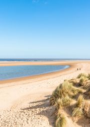 Sandy beach with grassy dunes and blue sky at the Norfolk Coast