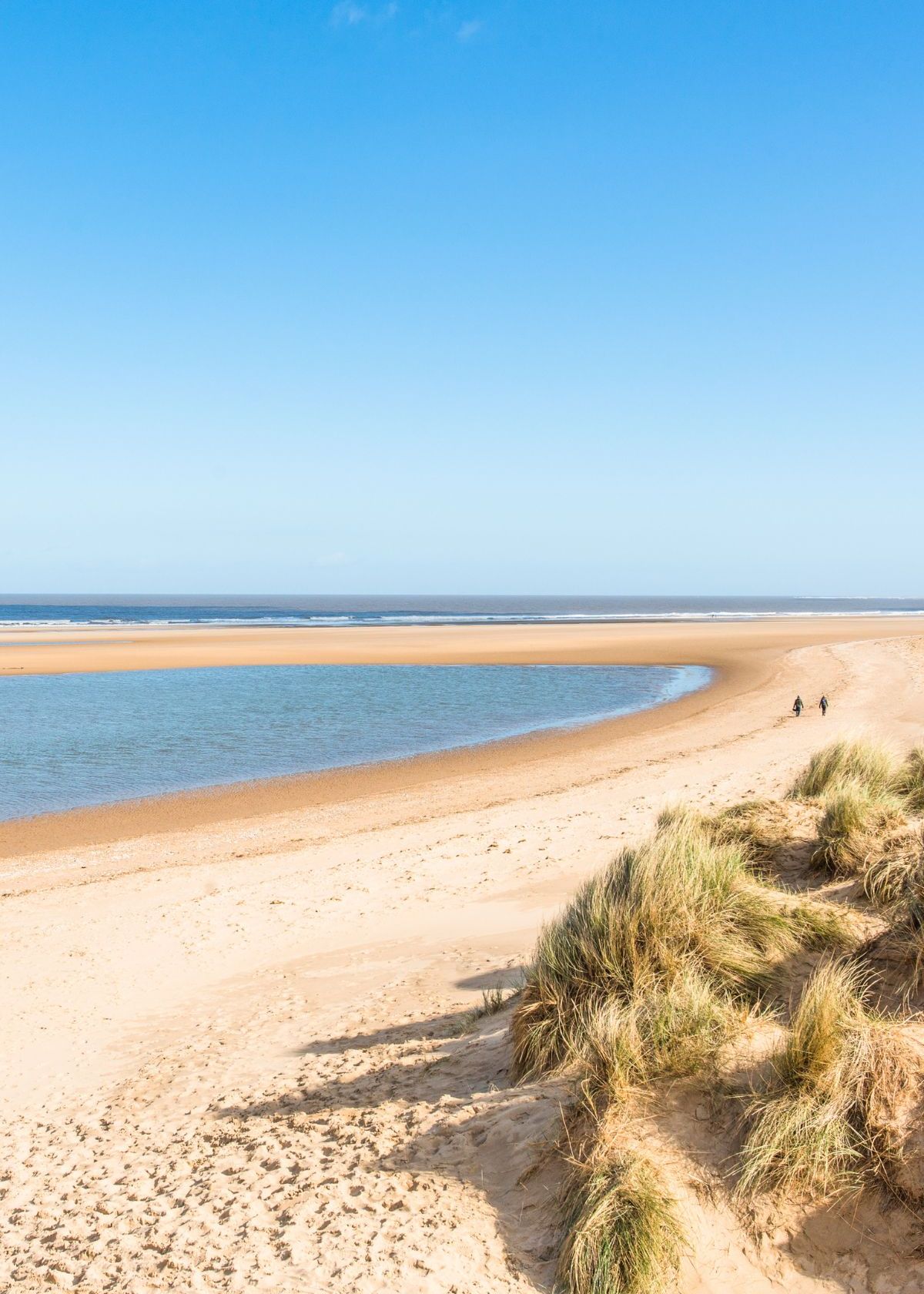 Sandy beach with grassy dunes and blue sky at the Norfolk Coast