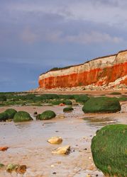 Norfolk coast with dramatic red and white cliffs, mossy rocks, and a sandy beach under a cloudy sky