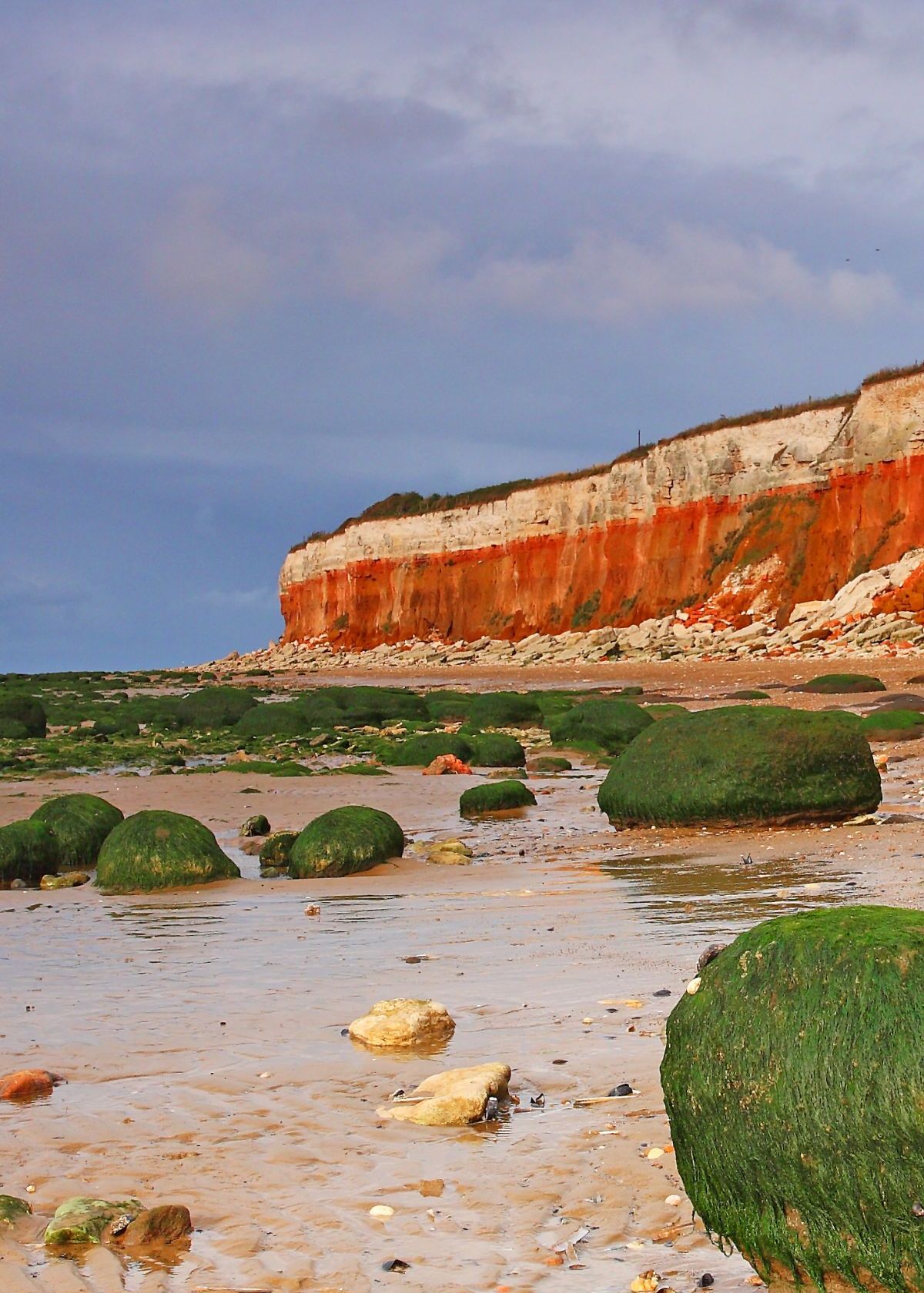 Norfolk coast with dramatic red and white cliffs, mossy rocks, and a sandy beach under a cloudy sky