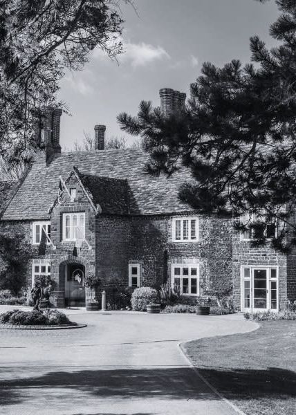 Black and white photo of Heacham Manor Hotel, a historic building with large windows and a gabled roof, surrounded by trees and landscaping.