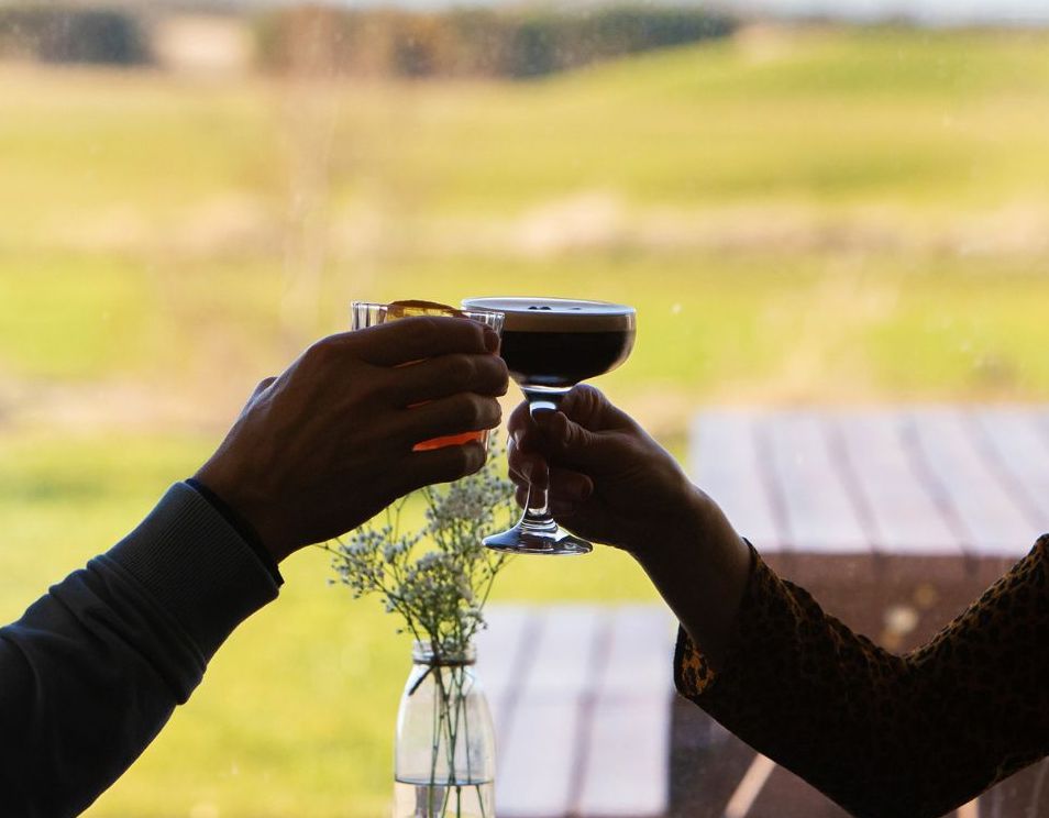 Two people toasting cocktails at a table with a golf course view in the background.