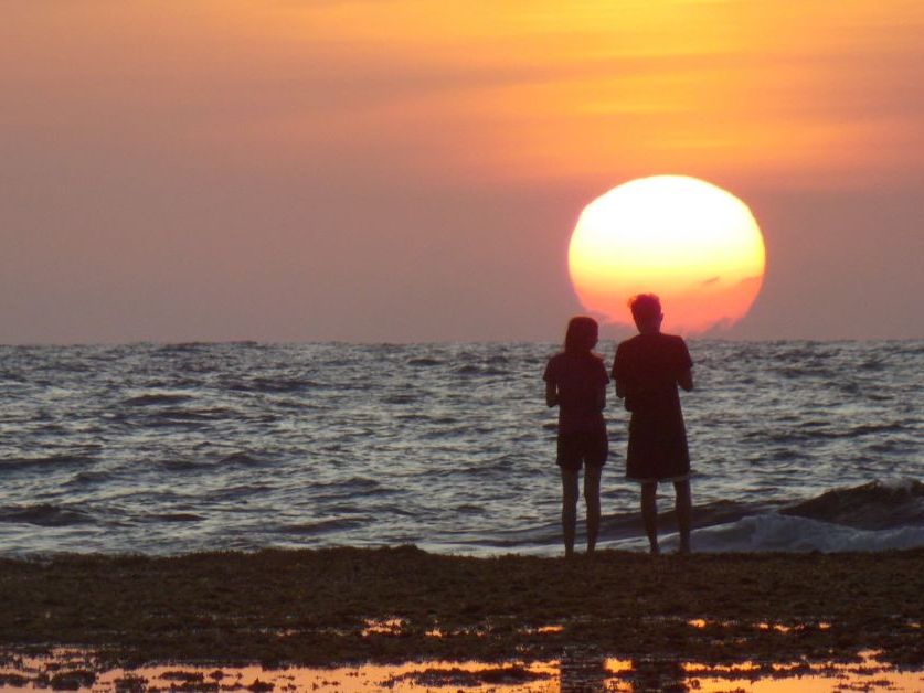 Silhouetted couple standing on a beach watching the sun set over the sea