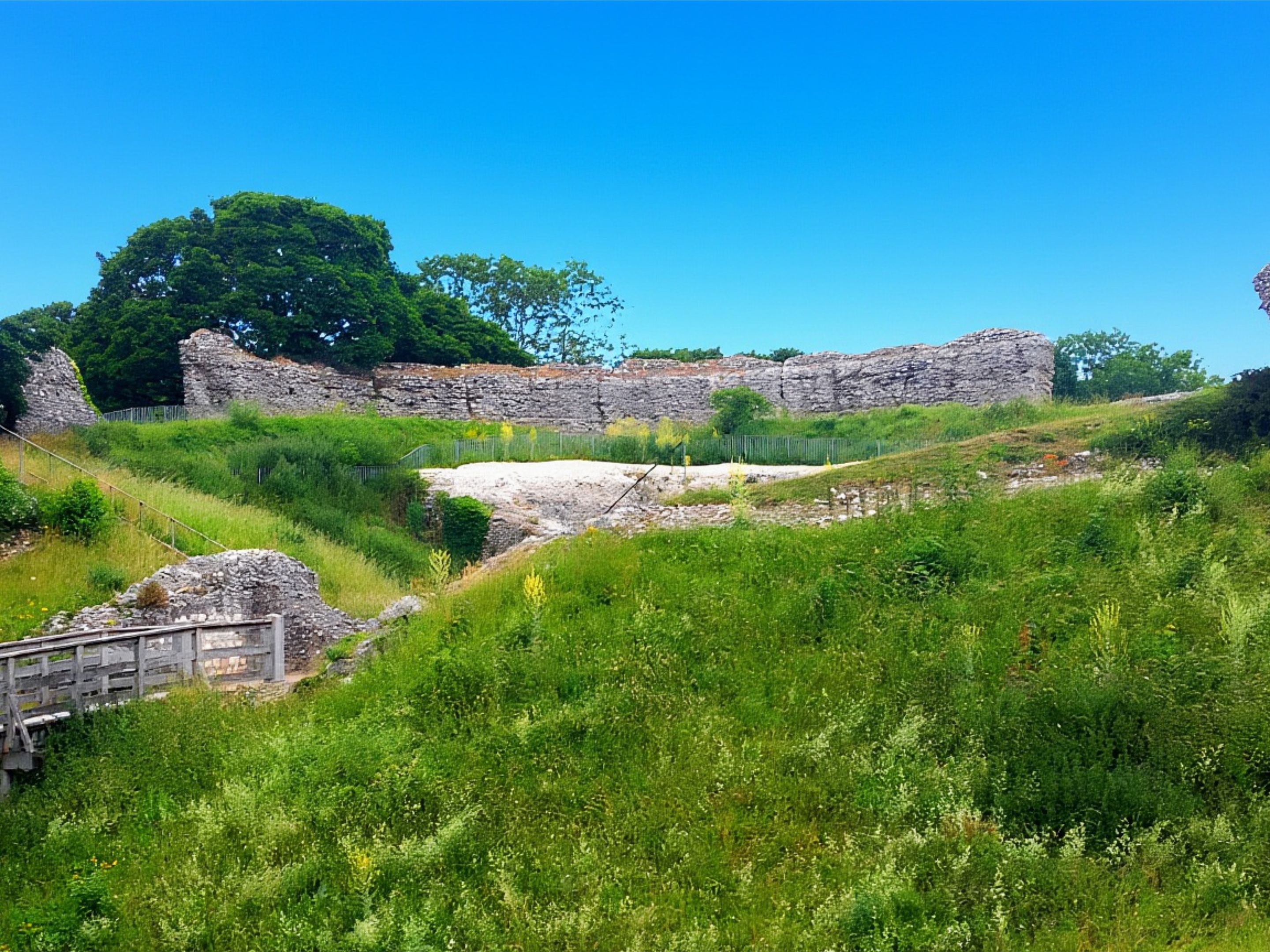 Stone ruins of Castle Acre Castle on a grassy hillside under a bright blue sky