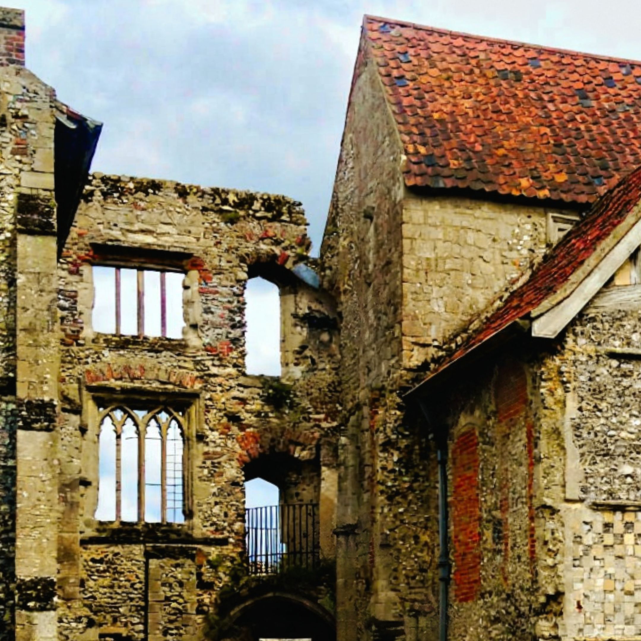 Stone ruins of Castle Acre Priory in Norfolk with a red-tiled roof and Gothic arched windows