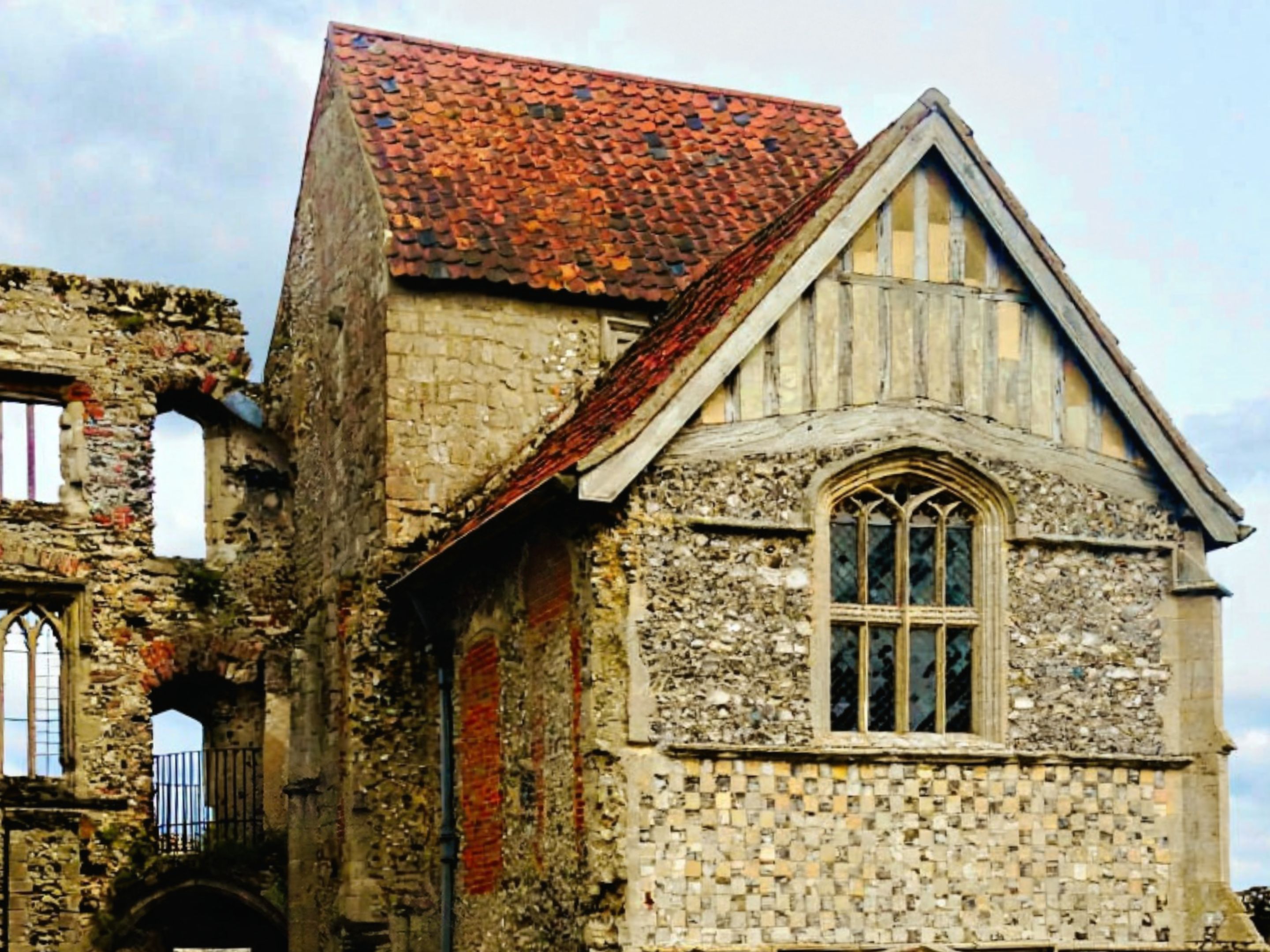 Stone ruins of Castle Acre Priory in Norfolk with a red-tiled roof and Gothic arched windows
