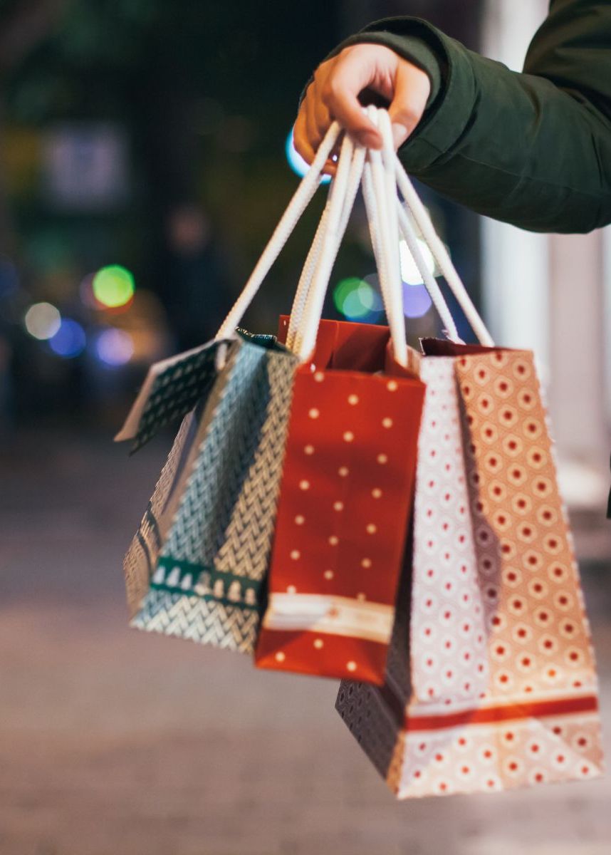 Person holding several patterned shopping bags on a city street at night with blurred festive lights in the background