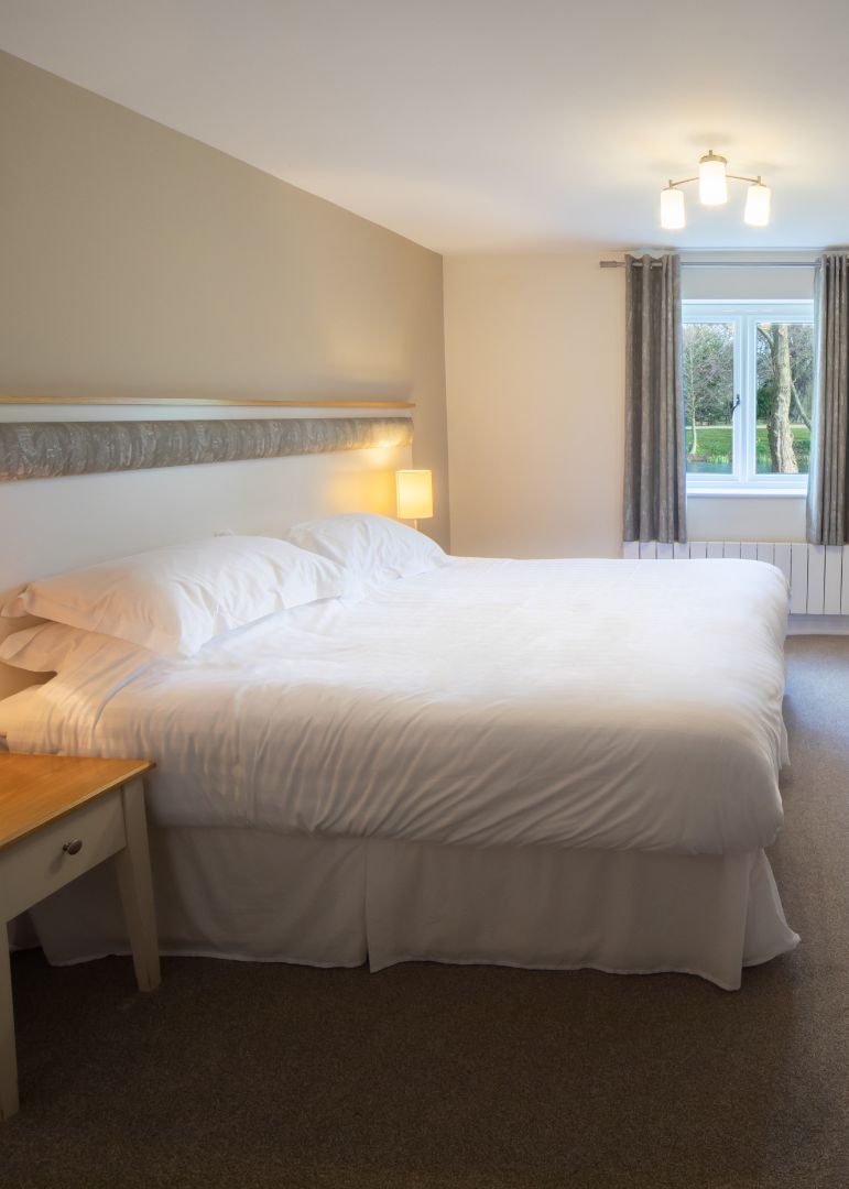 Bright cottage suite bedroom with double bed, bedside lamps, desk, chest of drawers and wall-mounted TV