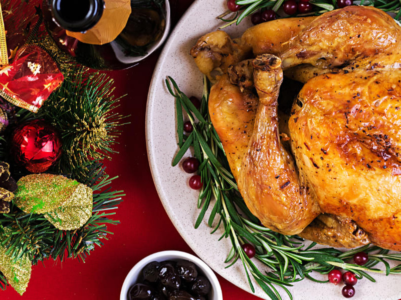 Roast Turkey garnishes with herbs on a red table with festive candleholder.
