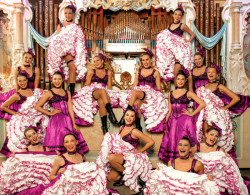 A troop of Can Can dancers dressed in pink in front of an ornate pipe organ.