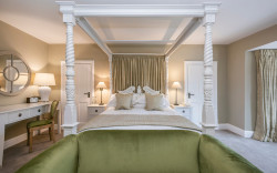 Luxurious hotel room decorated in neutral beige and white tones with a four poster bed and green velvet accents.
