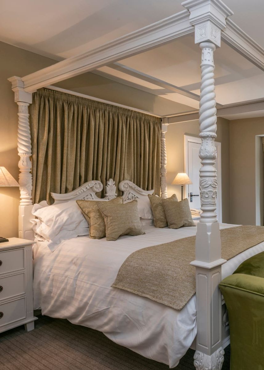Luxurious hotel room decorated in neutral beige and white tones with a four poster bed and green and mustard yellow velvet accents.