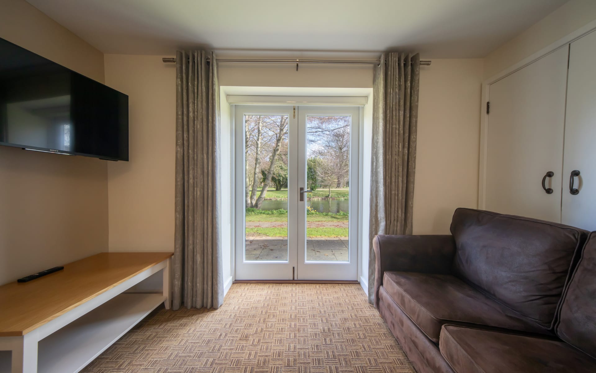 Lounge area with sofa, flat screen TV, coffee table and patio doors leading to outdoors.