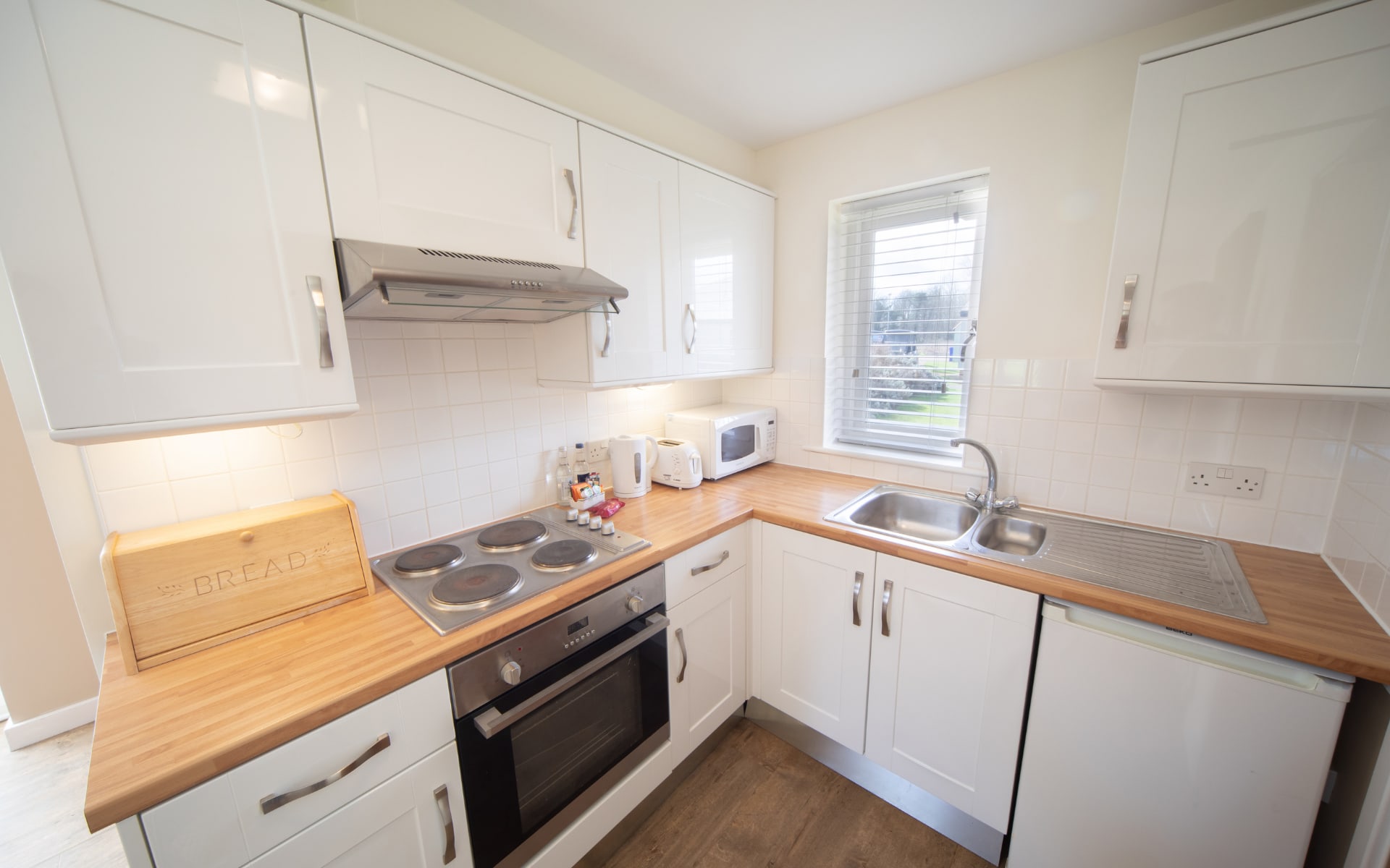 Kitchenette with sink, under counter fridge, oven and 4 ring burner. Decorated in a light colour palette.