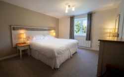 Hotel bedroom decorated in neutral tones with double bed and light coloured furniture.