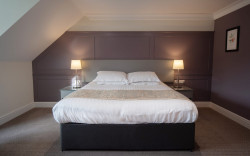 Kingsize Hotel Bed, with grey bedside tables, against a muted aubergine paneled wall.