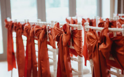 Wedding ceremony seating decorated in rich rust orange satin bows.