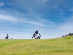 Golfers walking across a rolling course with wide open blue skies.