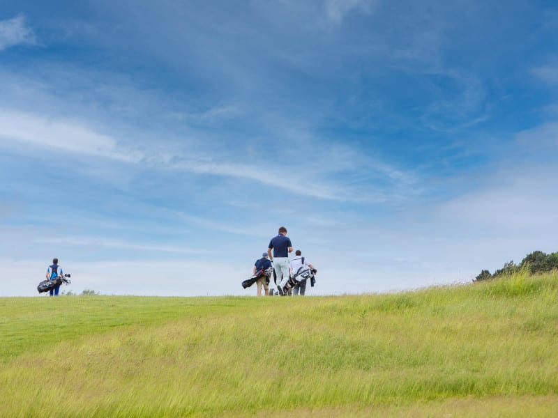 Golfers walking across a rolling course with wide open blue skies.