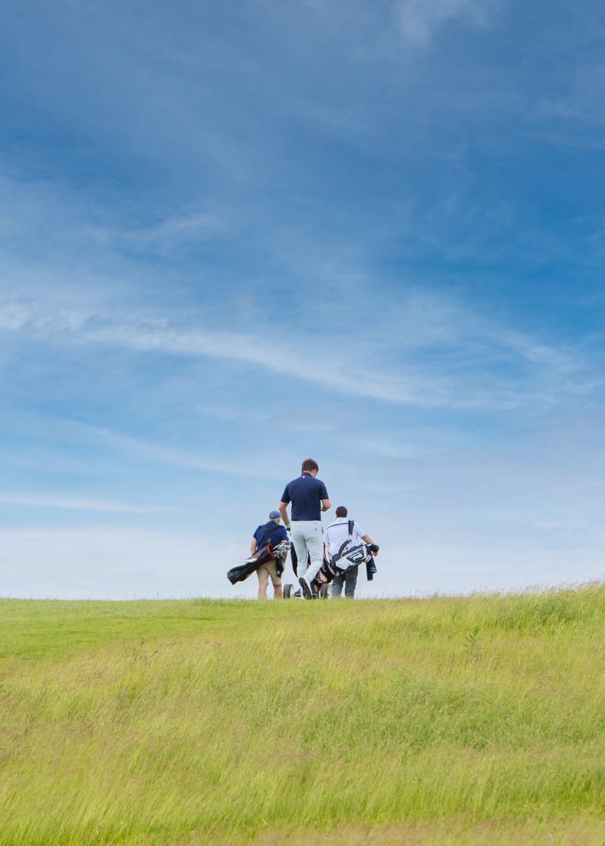 Golfers walking across a rolling course with wide open blue skies.