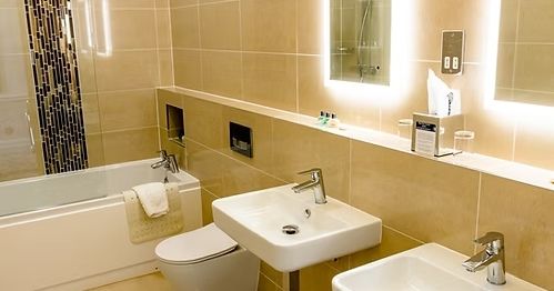 Modern bathroom with two sinks, a bathtub, toilet, and illuminated mirrors