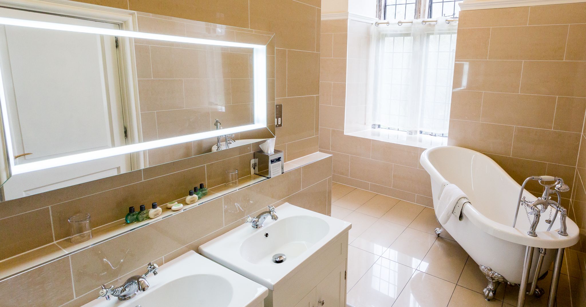 Modern bathroom with double sinks, a large illuminated mirror, and a freestanding bathtub