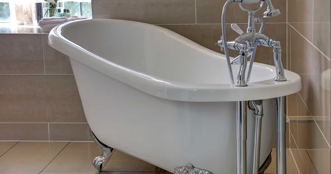 Freestanding clawfoot bathtub with chrome fixtures in a tiled bathroom.