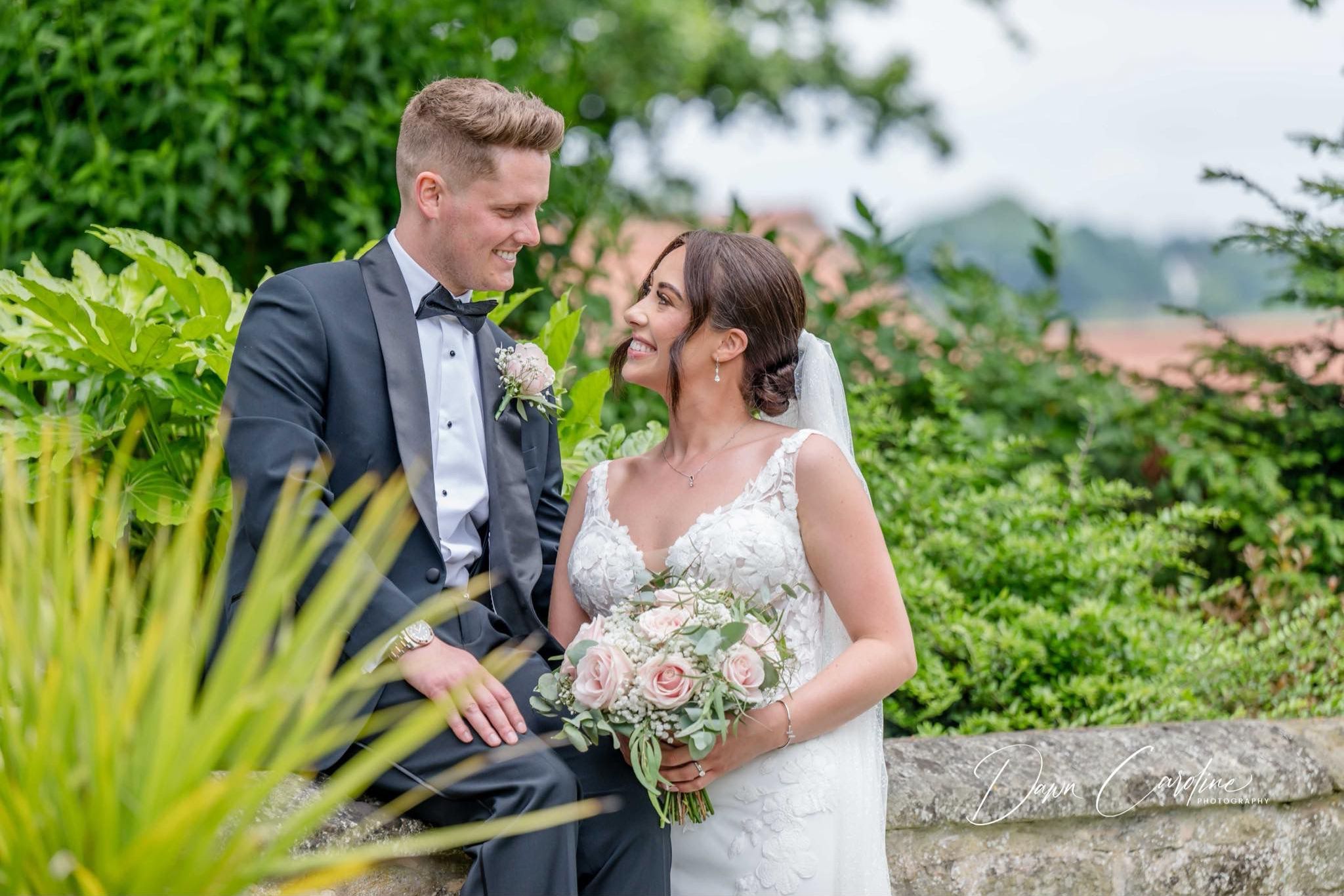 Bride and groom smiling at each other outdoors in a lush garden setting.