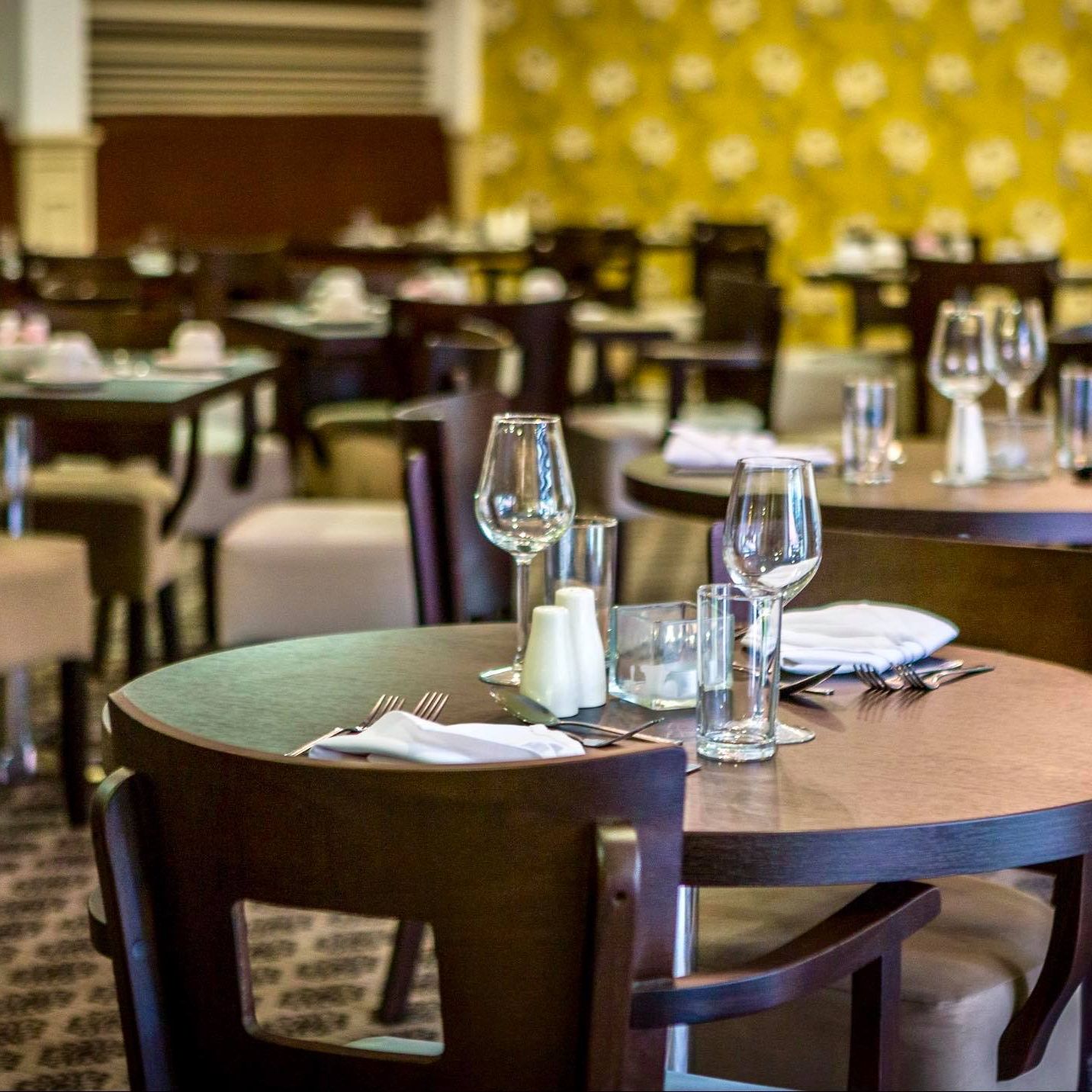Empty restaurant with round wooden tables set with wine glasses, plates, and cutlery