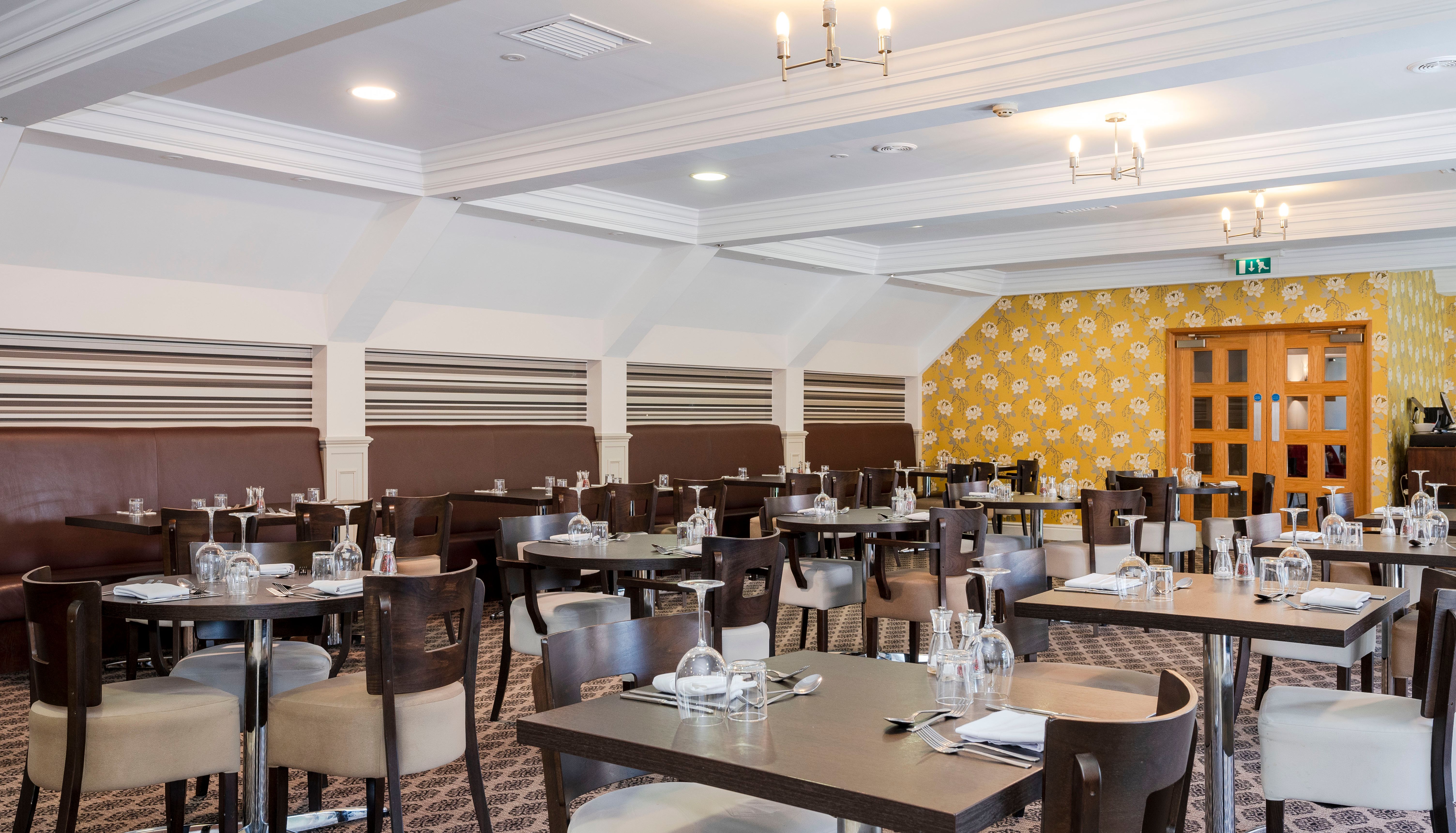 Modern restaurant dining area with multiple tables and chairs, set with glassware and utensils.