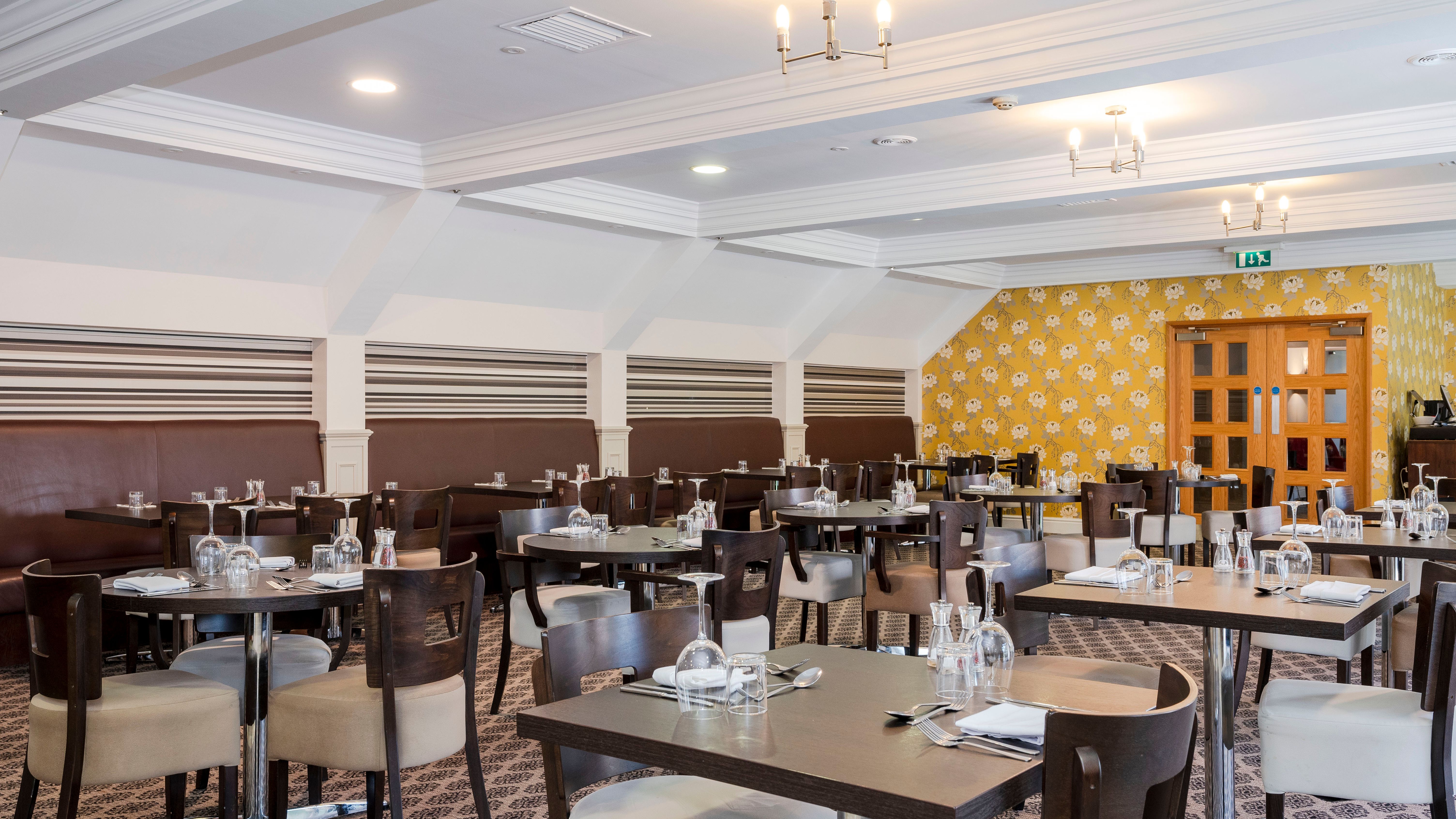 Modern restaurant dining area with multiple tables and chairs, set with glassware and utensils.