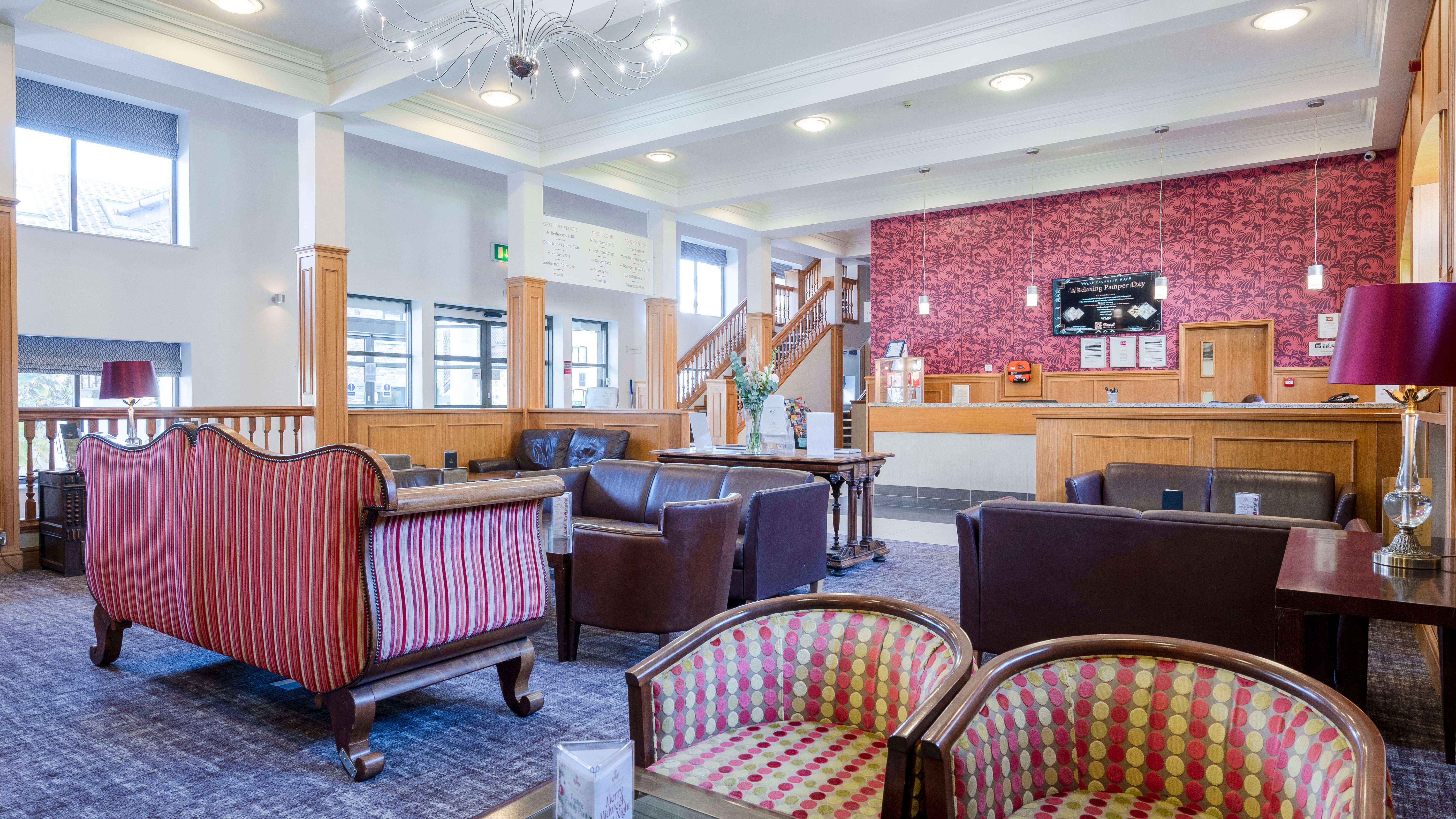 Bright hotel lobby with various seating areas, a chandelier, and a reception desk in the background.