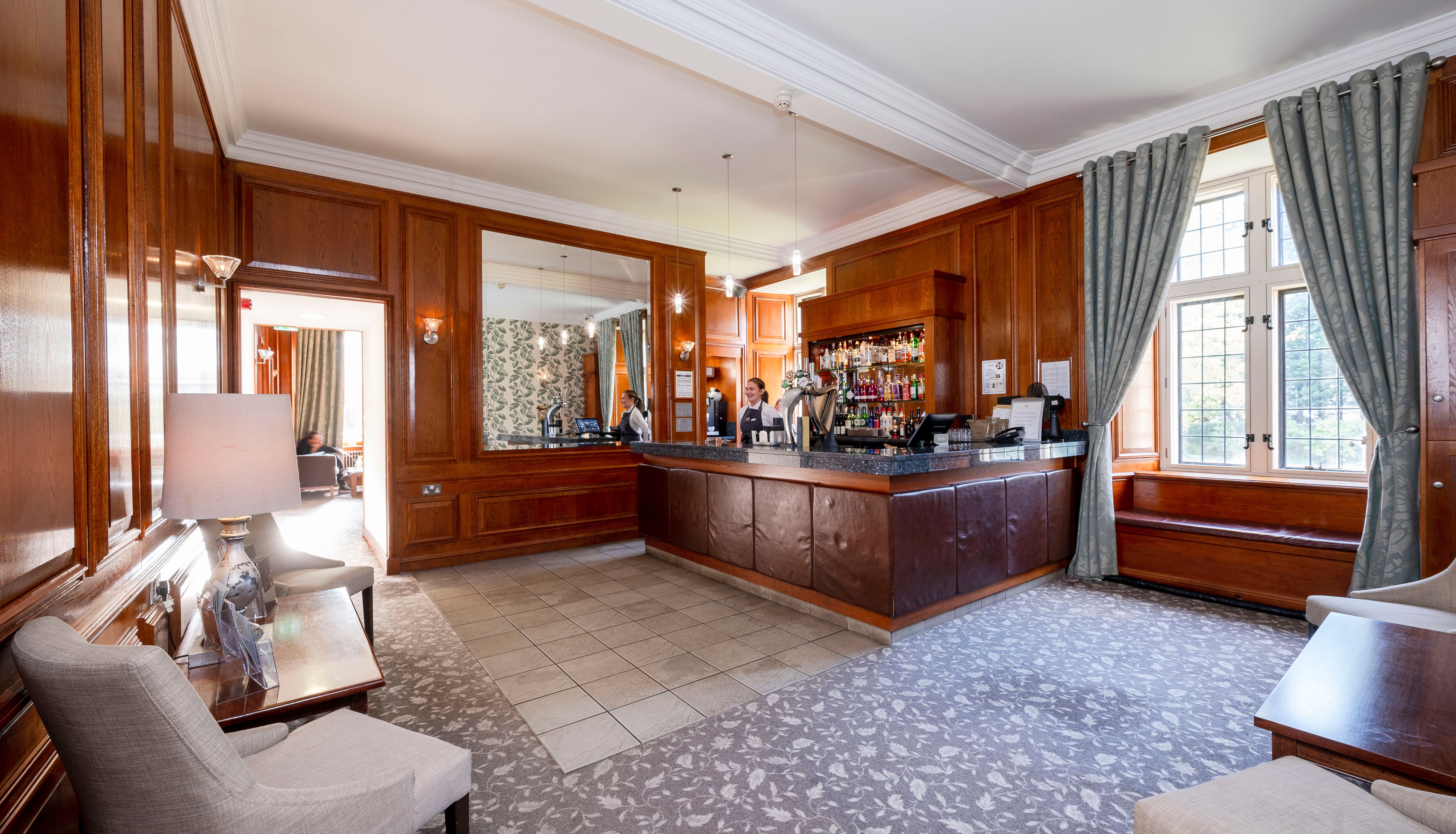 Elegant hotel bar area with wooden paneling, counter, and seating.