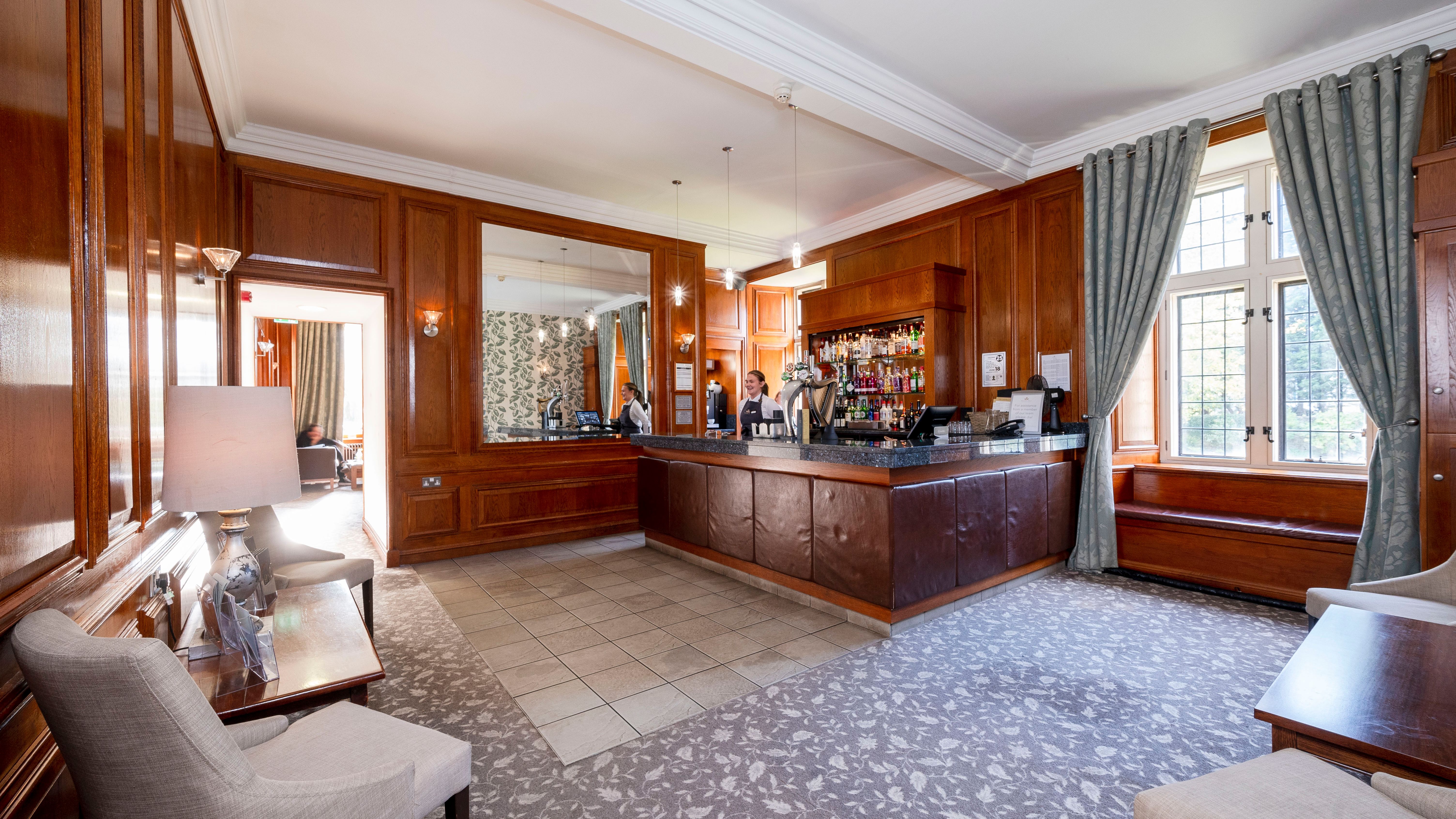 Elegant hotel bar area with wooden paneling, counter, and seating.
