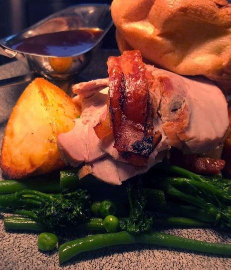 A plated roast dinner with sliced meat, roast potato, vegetables, Yorkshire pudding, and a gravy boat.