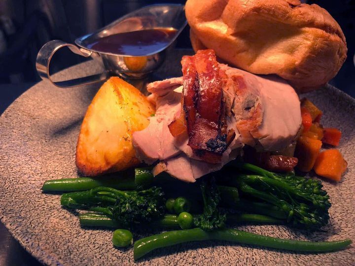 A plated roast dinner with sliced meat, roast potato, vegetables, Yorkshire pudding, and a gravy boat.