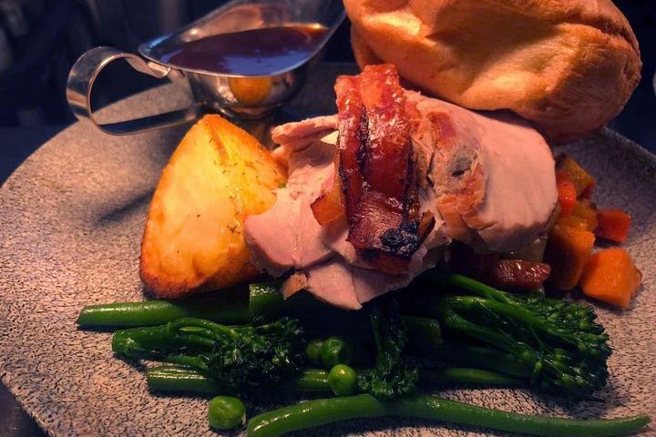 A plated roast dinner with sliced meat, roast potato, vegetables, Yorkshire pudding, and a gravy boat.