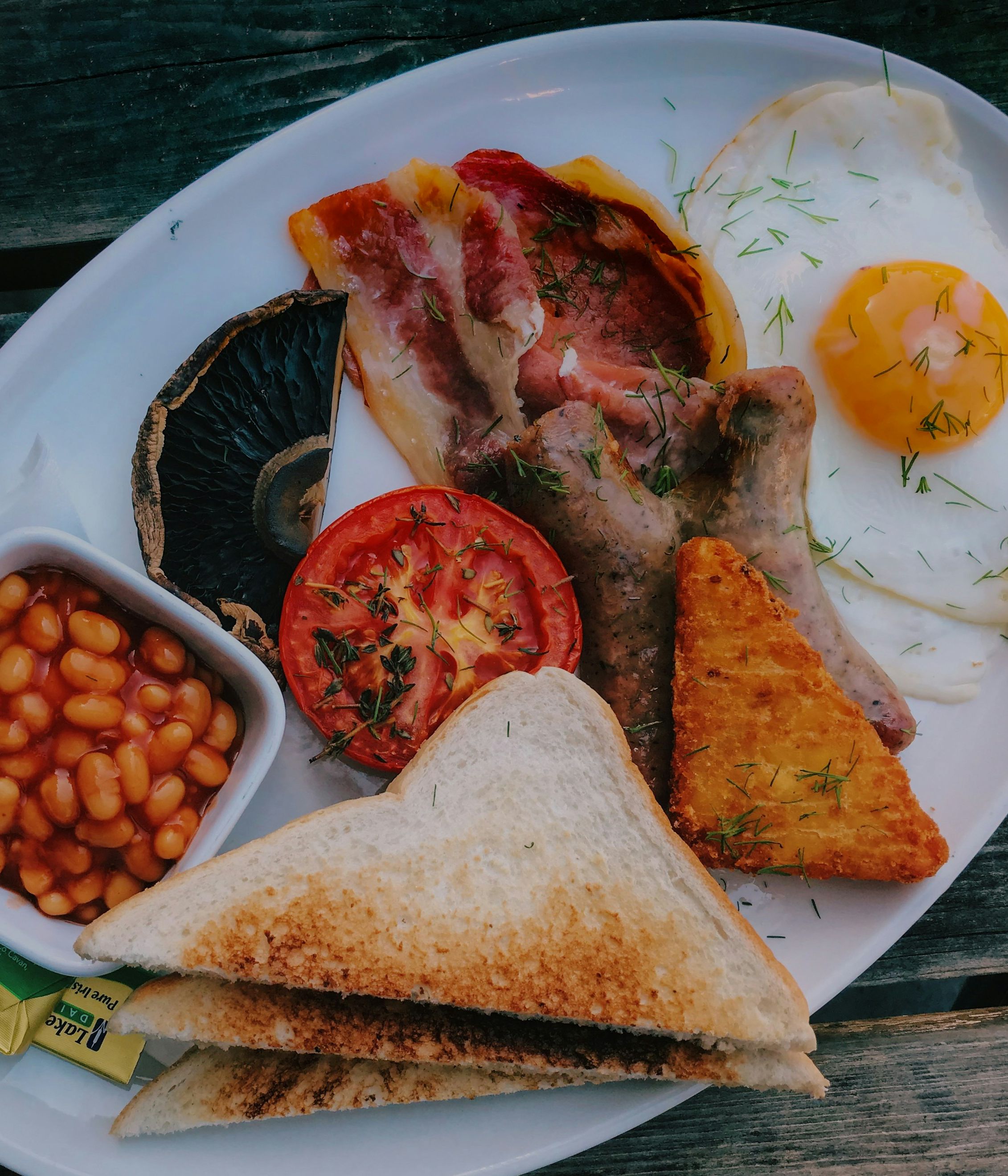 Traditional English breakfast with eggs, bacon, sausage, beans, tomato, mushroom, hash brown, toast, and a cup of coffee
